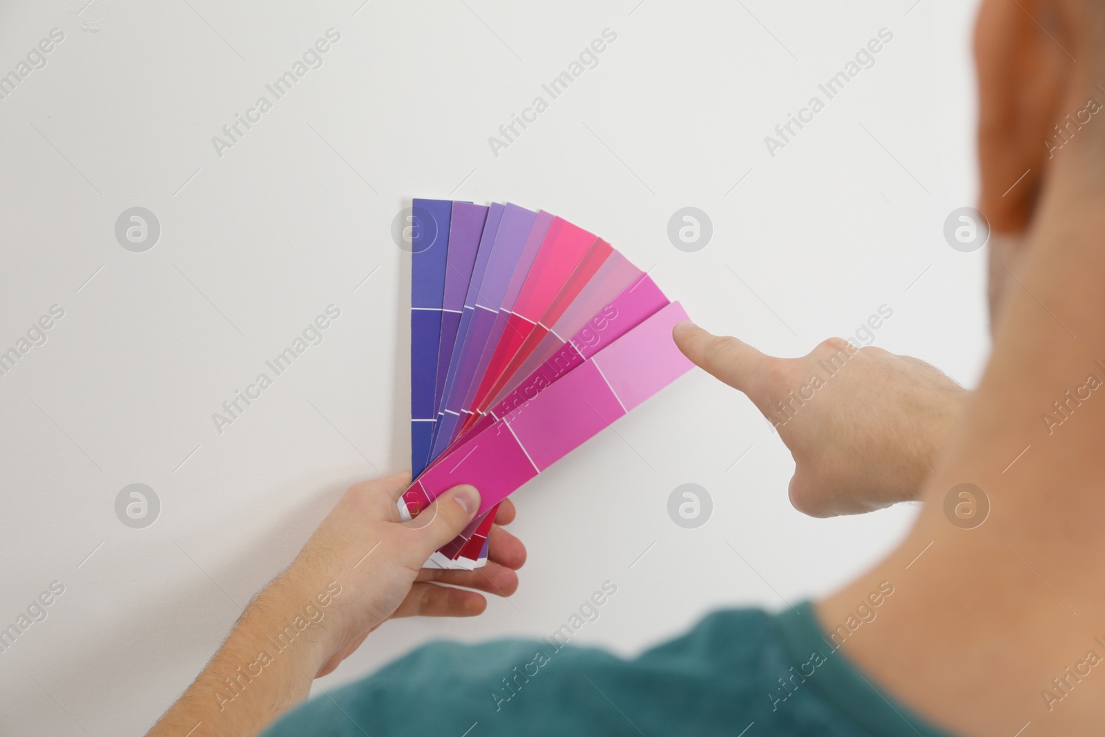 Photo of Man with palette choosing color for painting wall indoors, closeup. Interior design