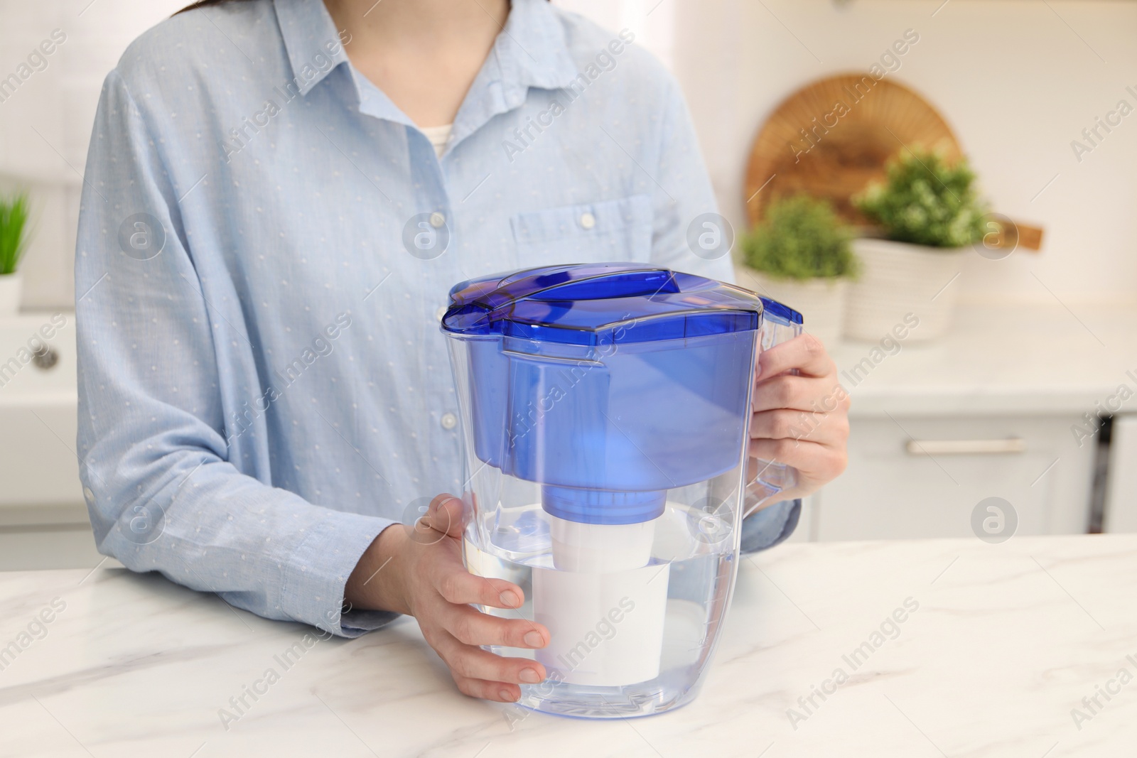 Photo of Woman with water filter jug at white marble table in kitchen, closeup. Space for text