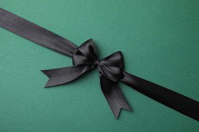 Photo of Black satin ribbon with bow on green background, top view