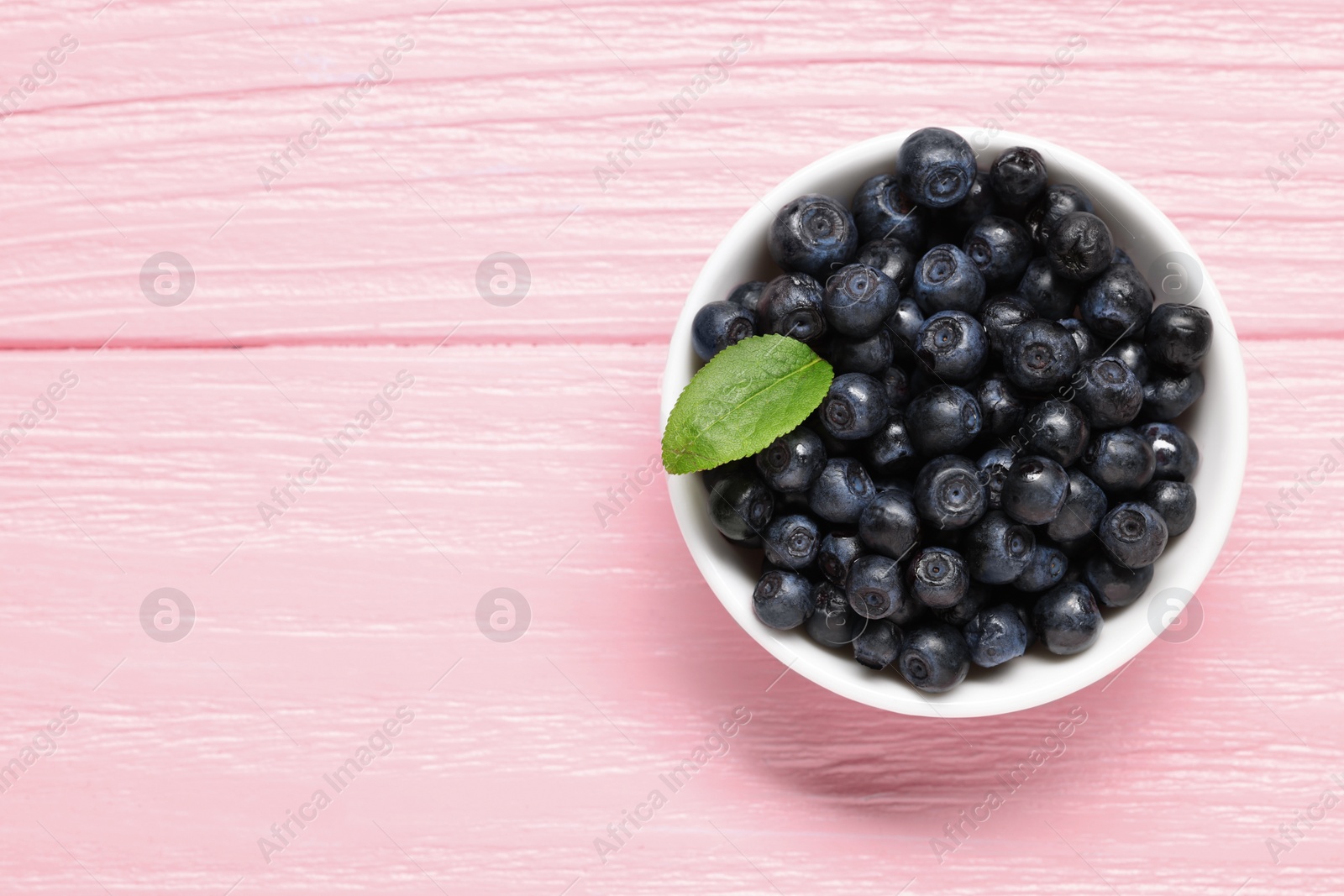 Photo of Tasty fresh bilberries in bowl on pink wooden table, top view. Space for text