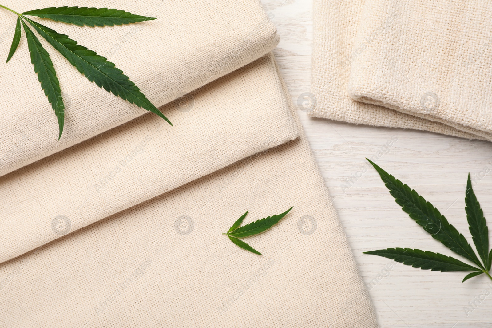 Photo of Hemp cloths and green leaves on white wooden table, flat lay