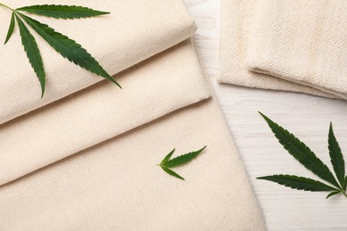 Photo of Hemp cloths and green leaves on white wooden table, flat lay