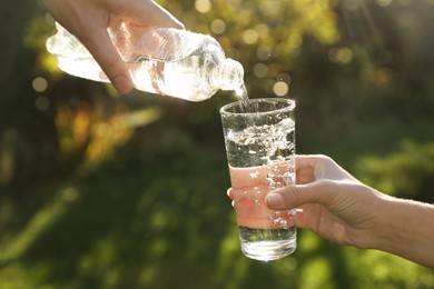 Photo of Man pouring fresh water from bottle into glass for woman outdoors, closeup