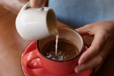 Photo of Woman adding milk to fresh aromatic coffee at table, closeup