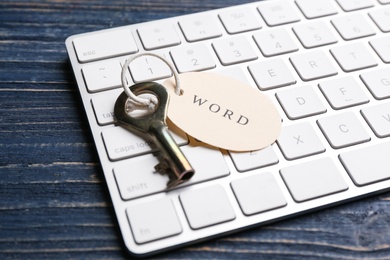 Photo of Key with tag WORD and computer keyboard on blue wooden table, closeup. Keyword concept