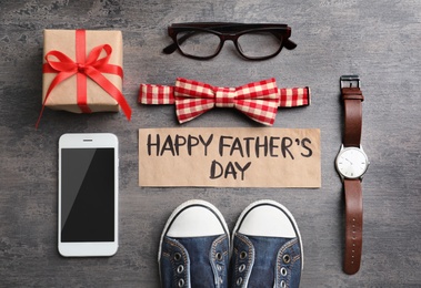 Photo of Small shoes, different gifts and card with words HAPPY FATHER'S DAY on wooden background, top view
