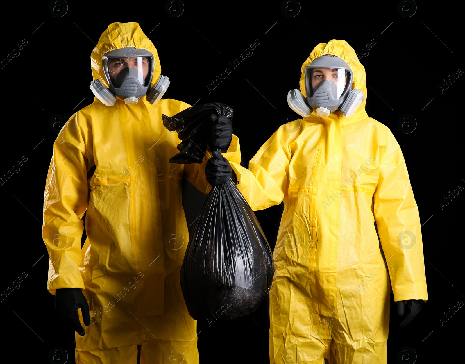 Photo of Man and woman in chemical protective suits holding trash bag on black background. Virus research