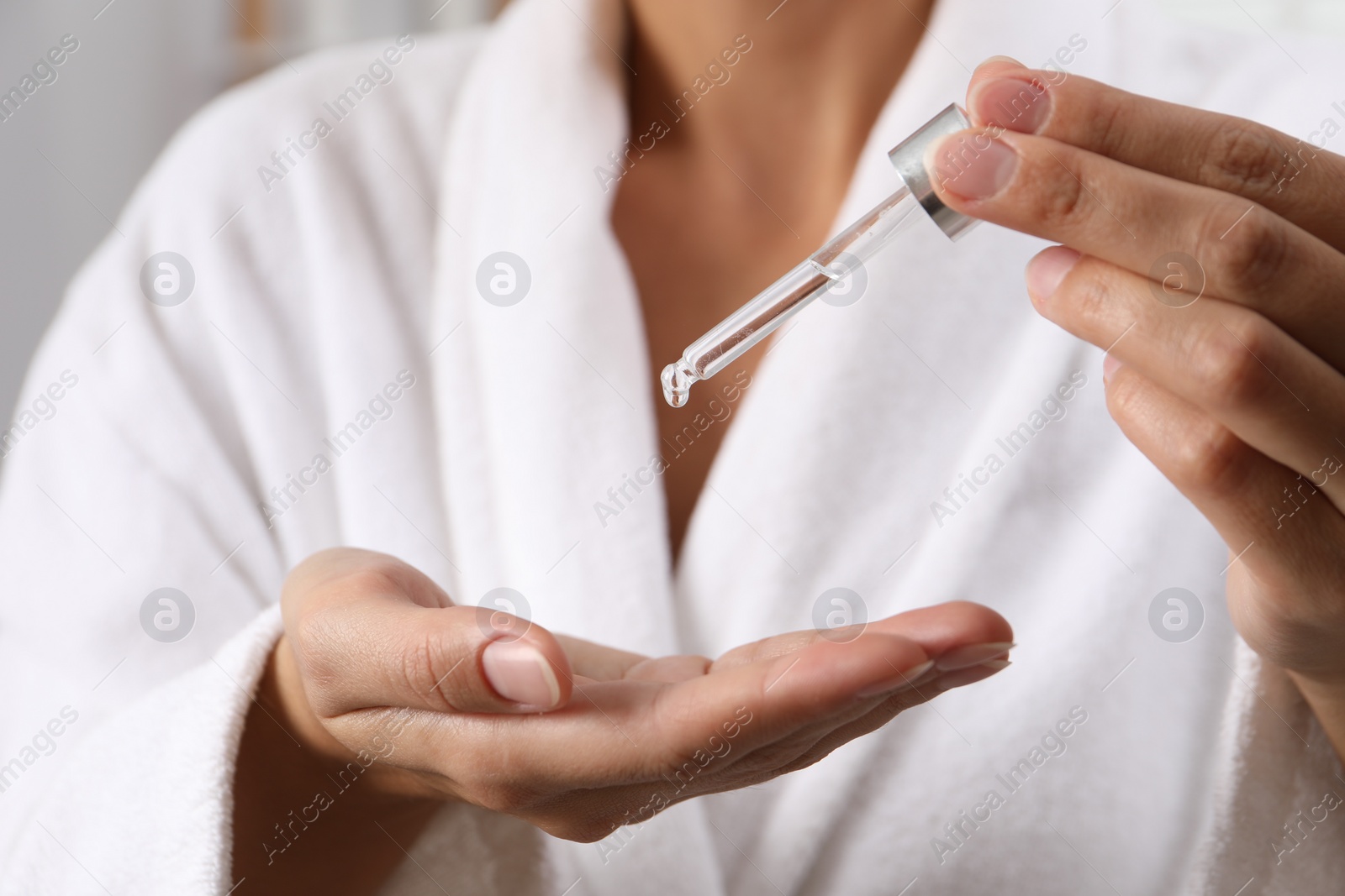 Photo of Woman applying cosmetic serum onto her hand on light background, closeup