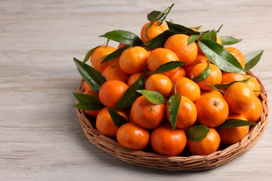 Photo of Fresh ripe juicy tangerines and green leaves on white wooden table. Space for text