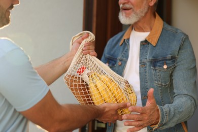 Photo of Man with net bag of products helping his senior neighbour outdoors, closeup