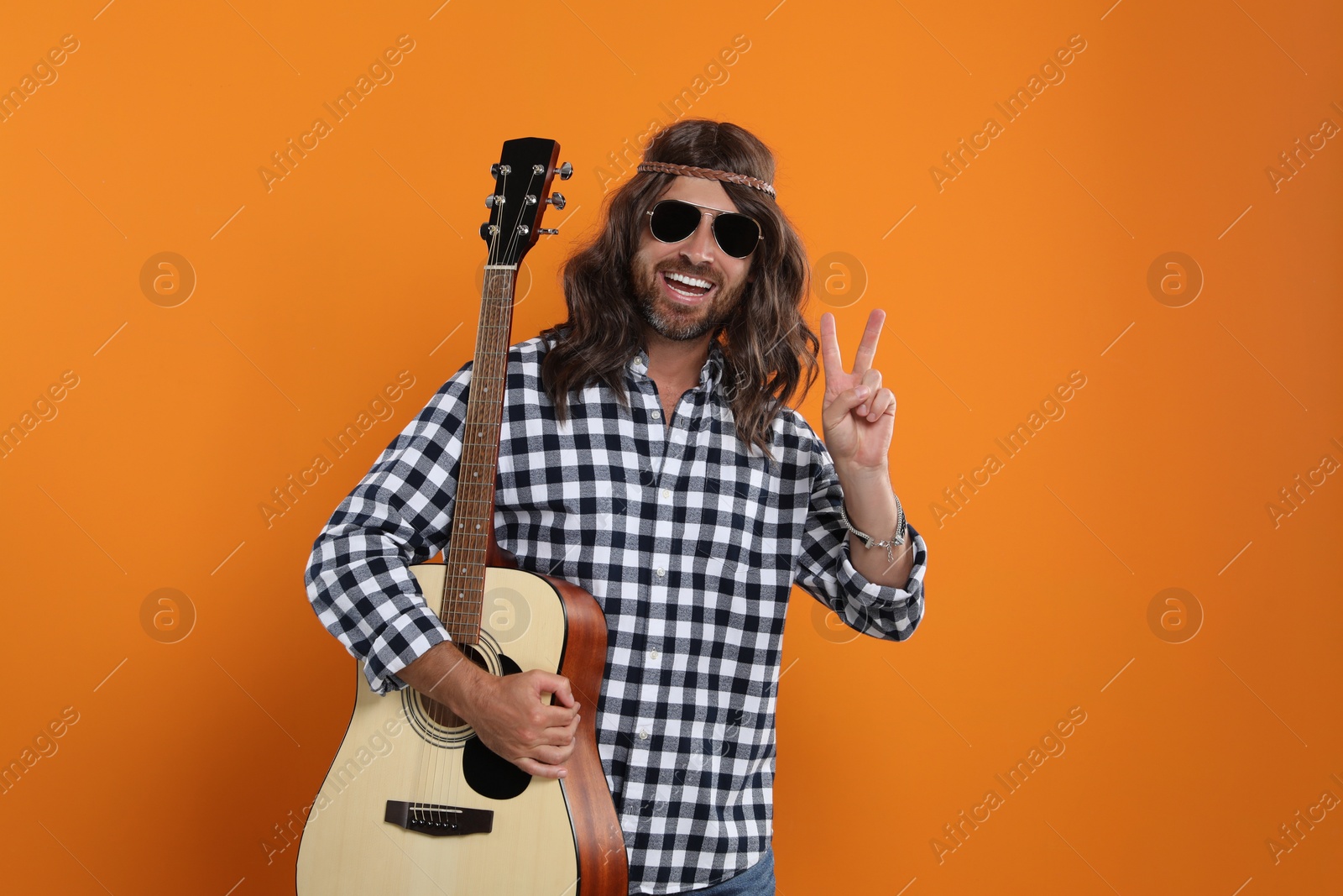 Photo of Hippie man with guitar showing V-sign on orange background