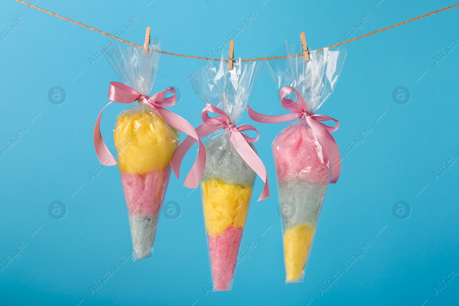 Photo of Packaged sweet cotton candies hanging on clothesline against light blue background