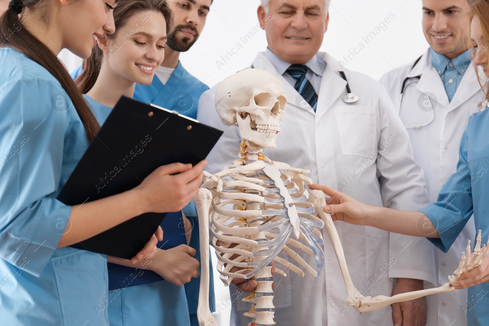 Photo of Professional orthopedist with human skeleton model teaching medical students in clinic