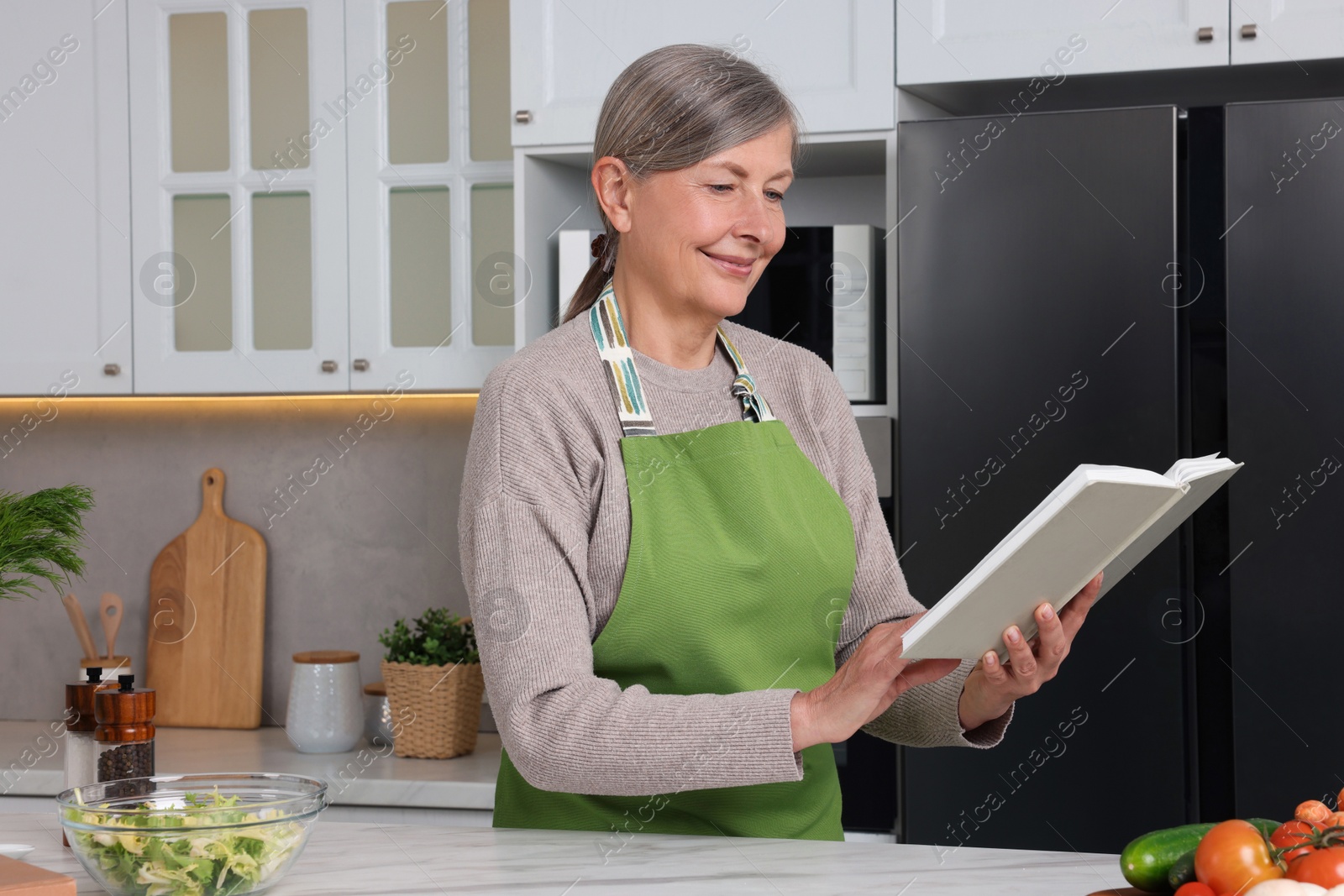 Photo of Happy woman with recipe book at table in kitchen