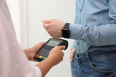 Photo of Man using smart watch for contactless payment via terminal indoors, closeup