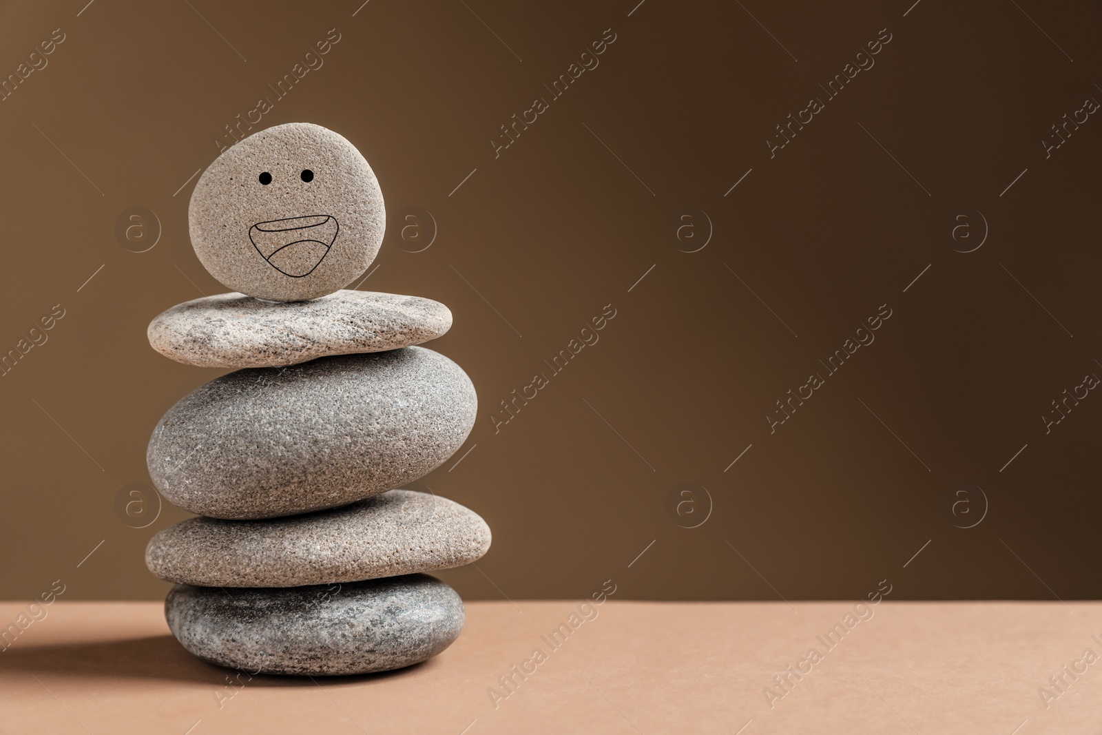 Photo of Stack of stones with drawn happy face on table against dark beige background, space for text. Zen concept