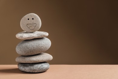 Photo of Stack of stones with drawn happy face on table against dark beige background, space for text. Zen concept