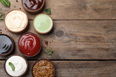 Photo of Many different sauces on wooden table, flat lay. Space for text
