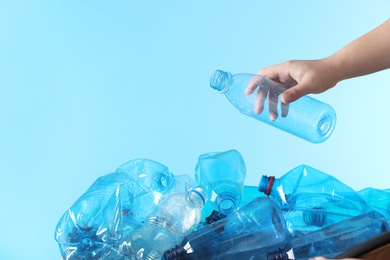 Photo of Woman putting used plastic bottle into cardboard box on color background, closeup with space for text. Recycling problem