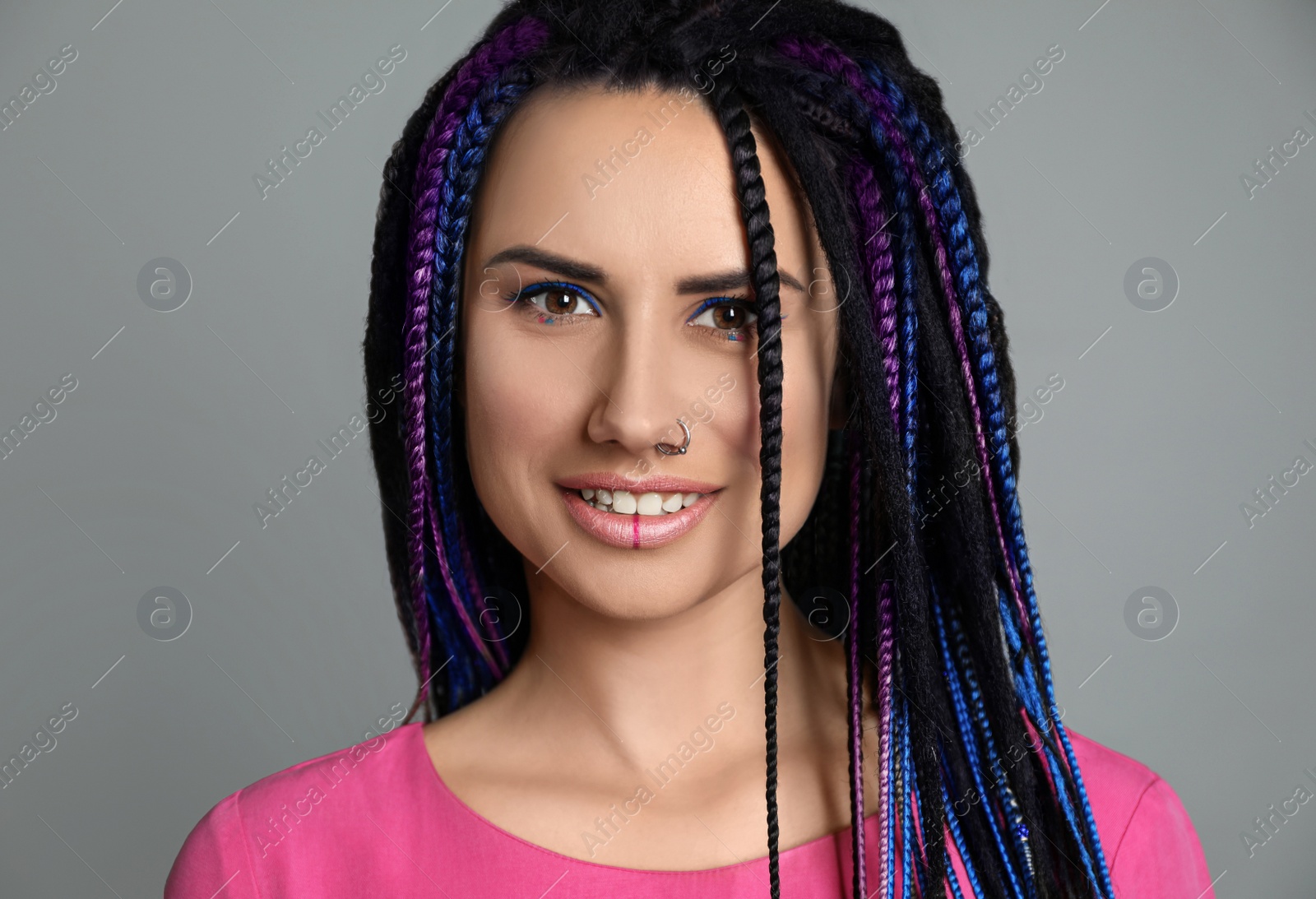 Photo of Beautiful young woman with nose piercing and dreadlocks on grey background