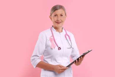 Photo of Doctor with pink ribbon, clipboard and stethoscope on color background. Breast cancer awareness