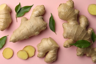 Photo of Fresh ginger with green leaves on pale pink background, flat lay