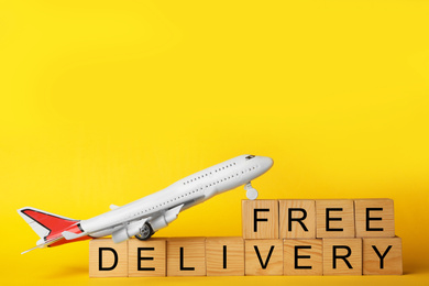 Photo of Toy plane and cubes with words FREE DELIVERY on yellow background. Logistics and wholesale concept