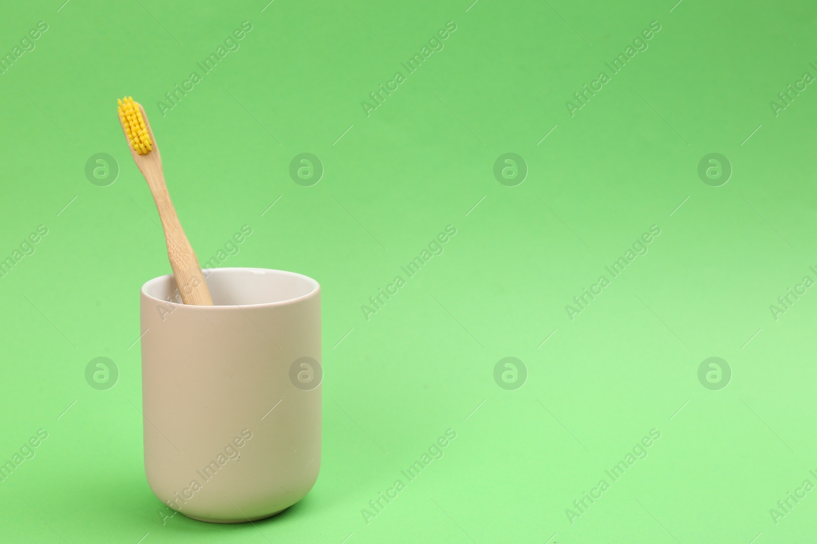 Photo of Bamboo toothbrush in holder on green background, space for text