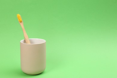 Bamboo toothbrush in holder on green background, space for text