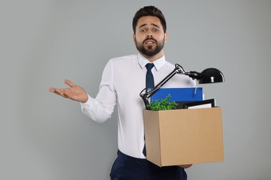 Photo of Confused unemployed man with box of personal office belongings on light grey background