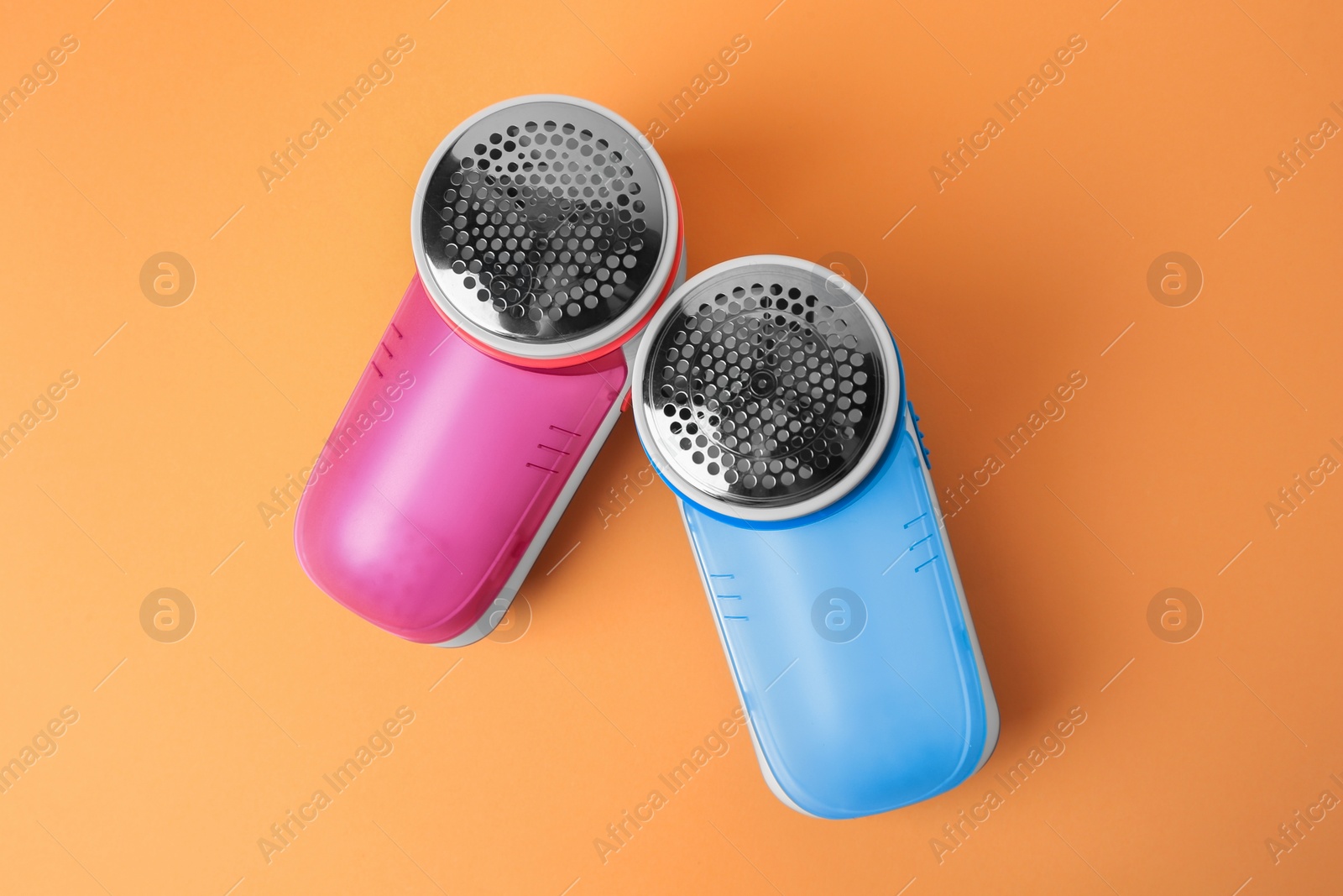 Photo of Modern fabric shavers on pale orange background, flat lay