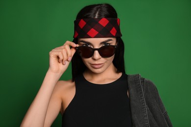 Photo of Fashionable young woman in stylish outfit with bandana on green background