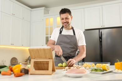 Photo of Happy man making dinner while watching online cooking course via tablet in kitchen