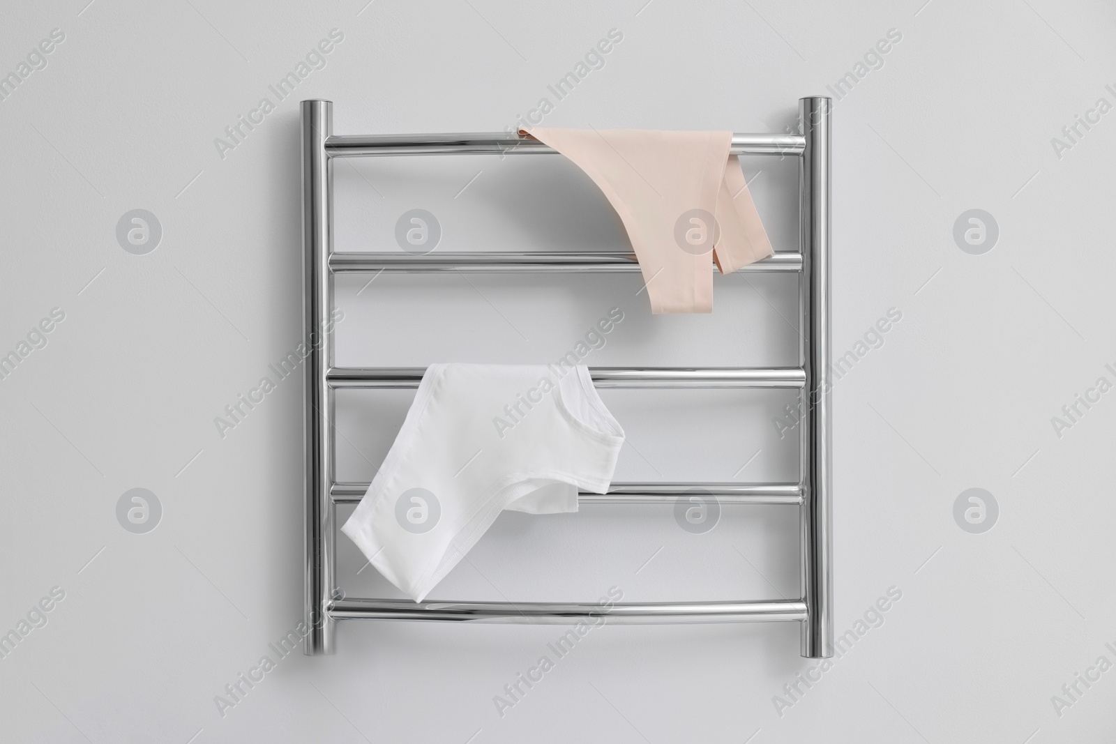 Photo of Heated towel rail with underwear on white wall in bathroom