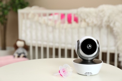 Modern CCTV security camera and pacifier on table in nursery. Space for text