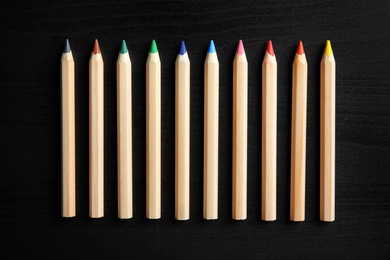 Photo of Pencils of different colors on wooden background, top view. School stationery