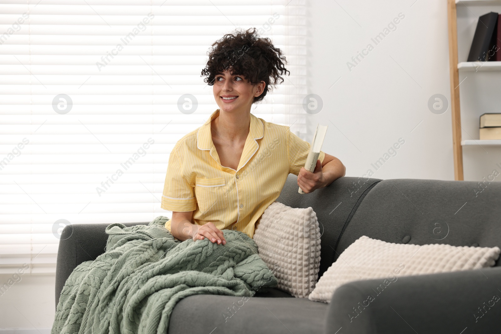 Photo of Beautiful young woman in stylish pyjama with book on sofa at home