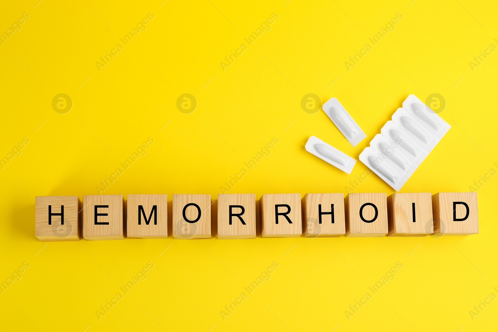 Photo of Wooden cubes with word HEMORRHOID and suppositories on yellow background, flat lay