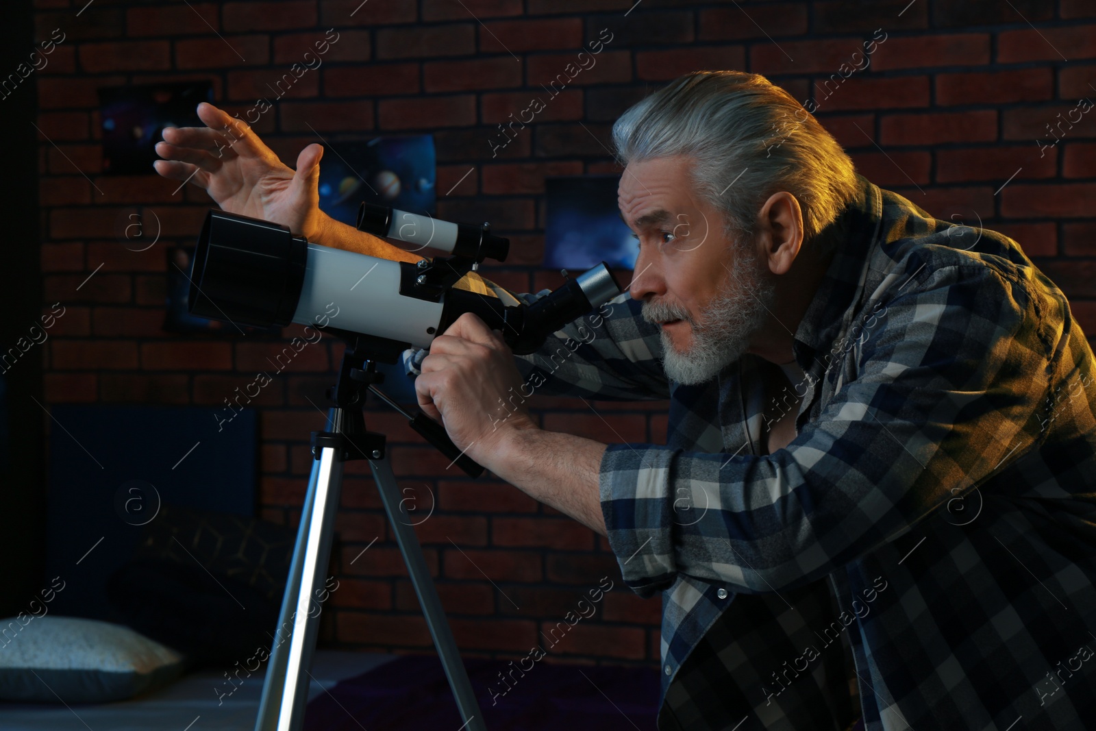 Photo of Senior man looking at stars through telescope in room