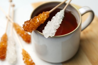 Photo of Sticks with sugar crystals and cup of tea on table, closeup