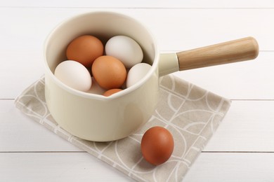 Unpeeled boiled eggs in pan on white wooden table, closeup