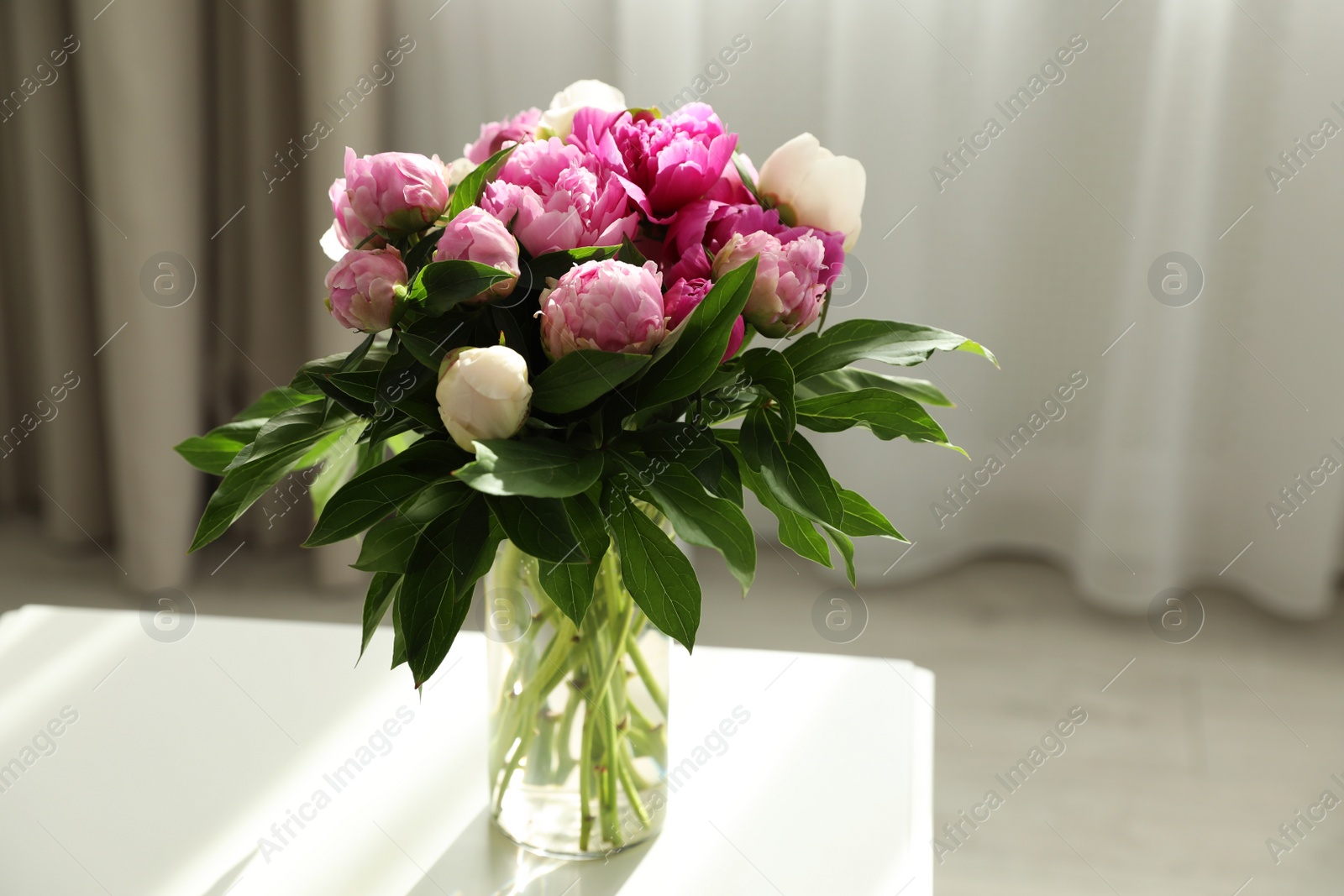 Photo of Vase with bouquet of beautiful peonies on table in room, space for text