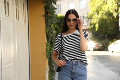 Photo of Beautiful young woman in stylish sunglasses walking on city street