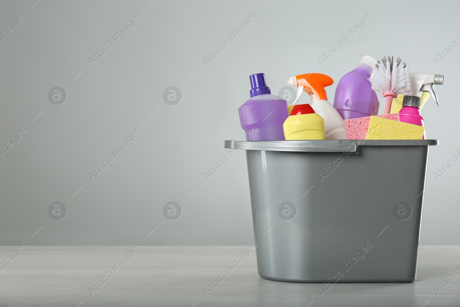 Photo of Bucket with different cleaning products and supplies on light table. Space for text