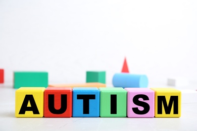 Colorful cubes with word AUTISM on table against light background