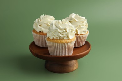 Tasty vanilla cupcakes with cream on green background