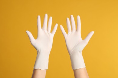 Photo of Doctor wearing medical gloves on yellow background, closeup