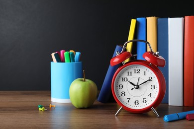 Alarm clock and different stationery on wooden table near blackboard. School time