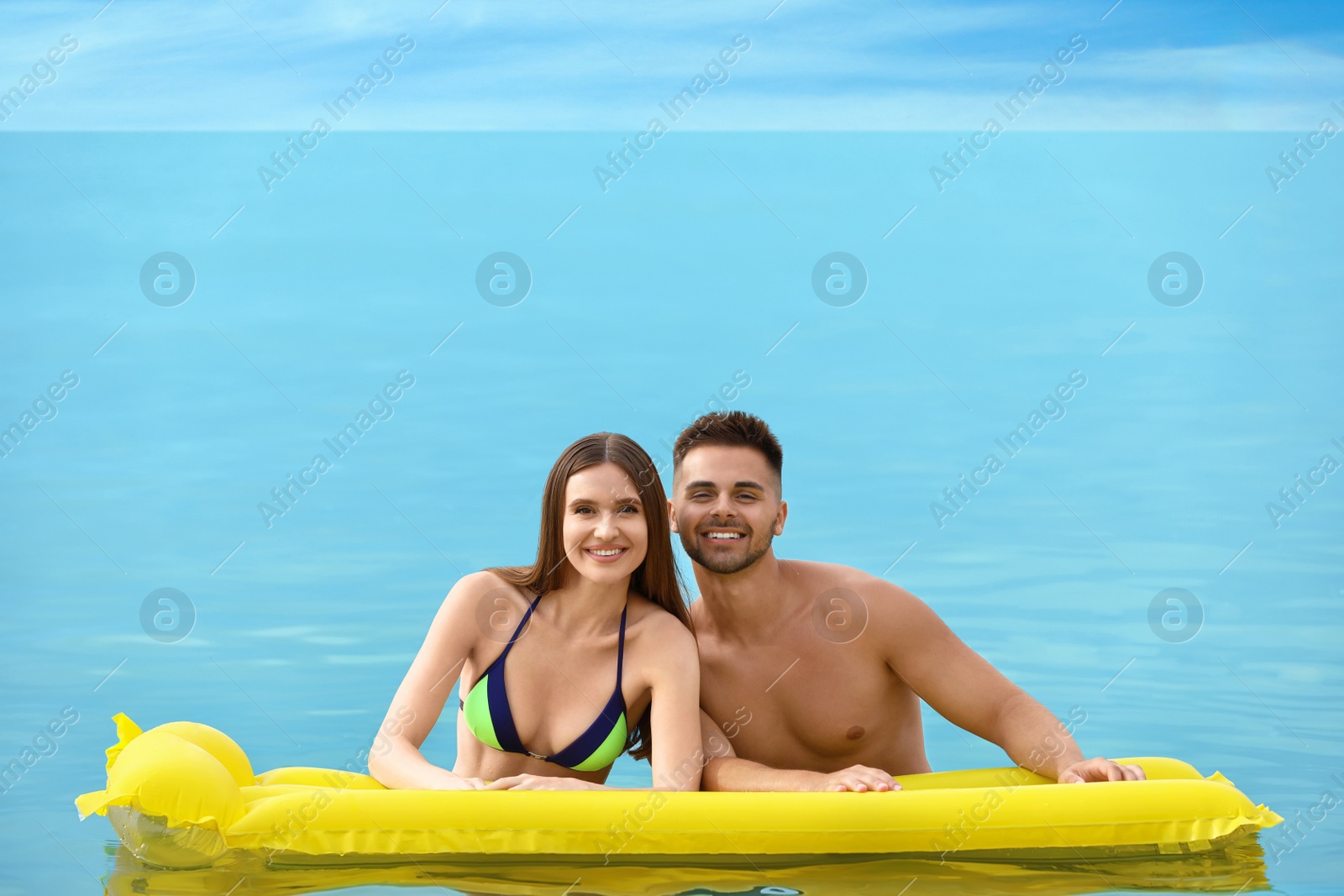 Photo of Young woman in bikini and her boyfriend with inflatable mattress in sea, space for text. Lovely couple