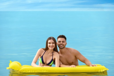 Young woman in bikini and her boyfriend with inflatable mattress in sea, space for text. Lovely couple